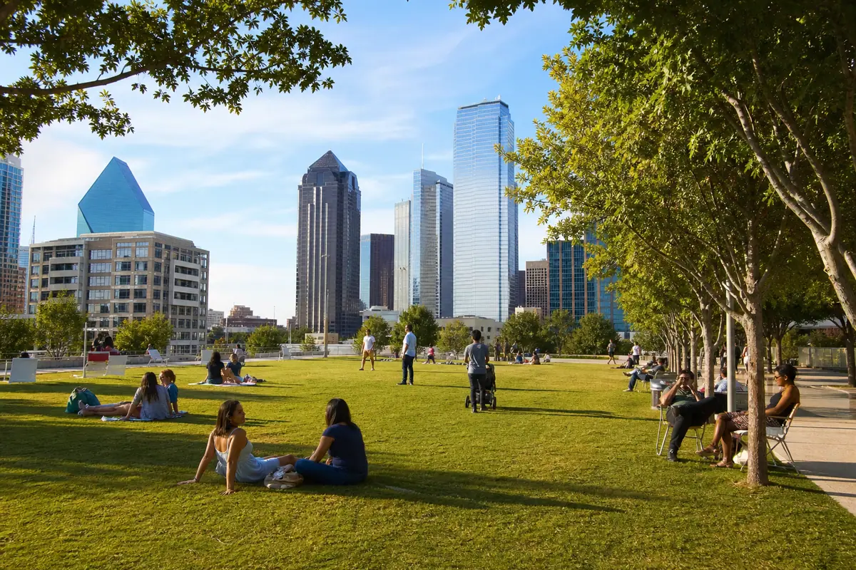 Photoreal Klyde Warren Park in Dallas with green lawn, skyline and relaxed urban activity